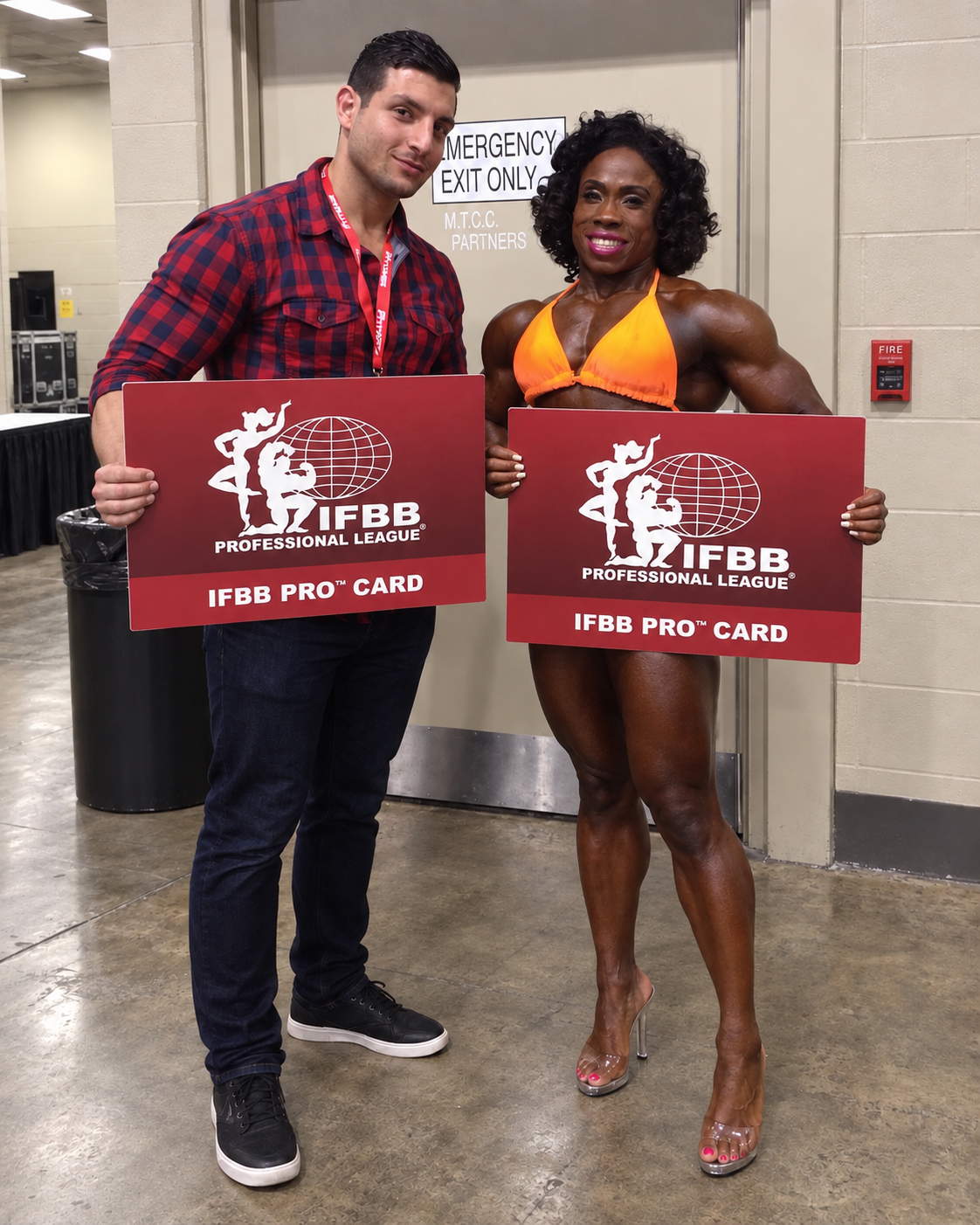 Hammer Fitness athlete backstage with coach Amer Kamra, holding her IFBB Pro card after turning professional